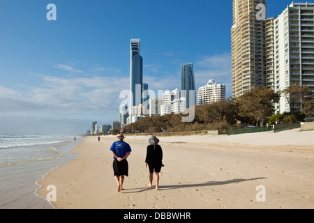 Giovane camminando lungo la spiaggia con vista sullo skyline in background. Surfers Paradise, Gold Coast, Queensland, Australia Foto Stock