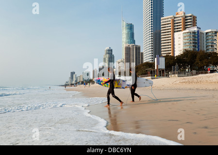 I surfisti a piedi in surf con skyline della città in background. Surfers Paradise, Gold Coast, Queensland, Australia Foto Stock