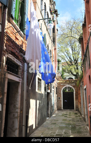 Piccola strada con lenzuola blu appese ad asciugare il giorno di sole fuori case a Venezia, Venezia, Veneto, Italia, Europa Foto Stock
