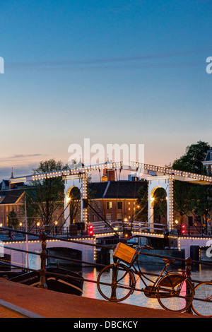 Amsterdam Magere Brug, Skinny, il ponte sul fiume Amstel e Museo Hermitage al crepuscolo e di notte sera in estate biciclette parcheggiate Foto Stock