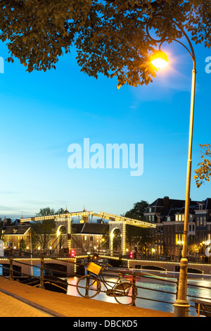 Amsterdam Magere Brug Skinny ponte sul fiume Amstel crepuscolo serale di notte in estate. Una sola bicicletta è bloccato alla ringhiera. Foto Stock