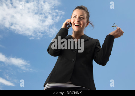 Donna d'affari sorridente che parla con uno smartphone all'esterno Foto Stock