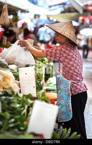 La donna nel cappello conico lavorando a un vegetale stallo a Graham Street mercato umido, Isola di Hong Kong Foto Stock