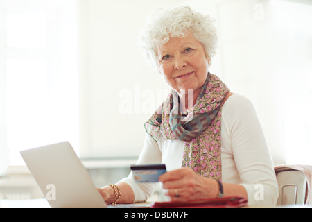 Sorridente signora matura in possesso di una carta di credito di fronte il suo computer portatile Foto Stock