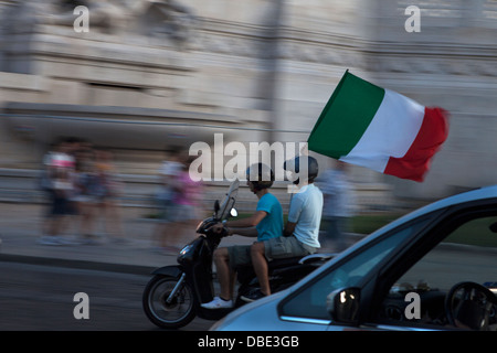 Due giovani passeggiate in bicicletta con una bandiera italiana prima di una partita di calcio. Foto Stock