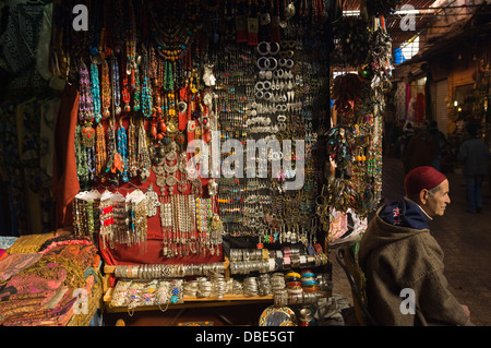 Custode di stallo mantenendo guarda per i clienti di fronte al suo negozio di vendita gioielli, nel souk di Marrakech, Marocco Foto Stock