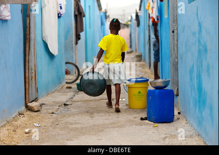 Una ragazza con una ciotola passeggiate lungo un vicolo tra case colorate in La soluzione salina, Port-au-Prince, Haiti Foto Stock