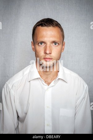 Giovane uomo gravi in maglia bianca su sfondo grigio. Ritratto in studio Foto Stock