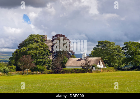 St.Marys Chiesa e cottage con il tetto di paglia a Bratton Clovelly in Devon occidentale sotto un cielo tempestoso con Dartmoor nel lontano sullo sfondo. Foto Stock