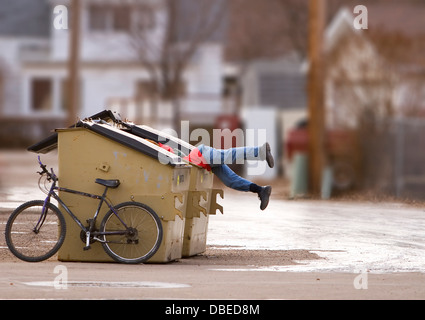 Uomo senza tetto con una bici cerca in un cassonetto Foto Stock