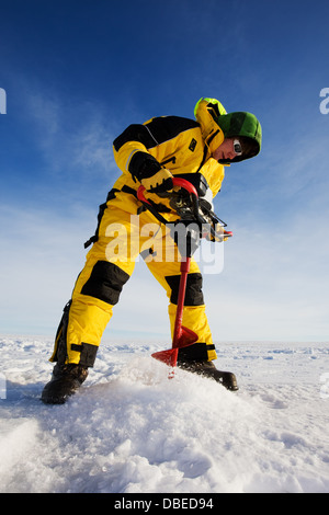 Pescatore di ghiaccio la trapanatura di un foro su un lago ghiacciato con una coclea di alimentazione Foto Stock