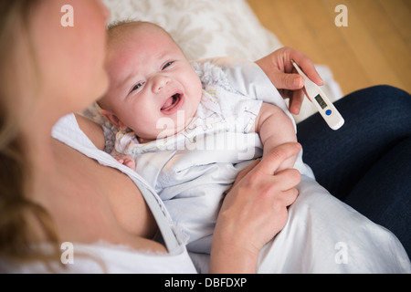 Madre caucasica tenendo il pianto temperatura del bambino Foto Stock