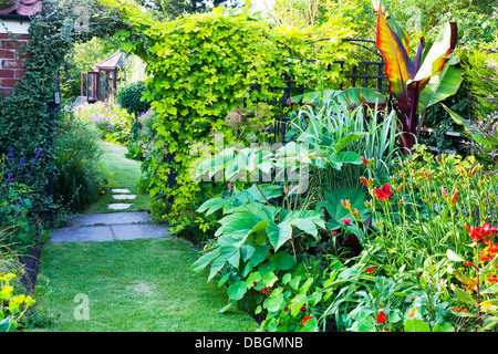 Tipico giardino inglese piante fiori piantati a lato del percorso che conduce attraverso arch a casa estiva Foto Stock