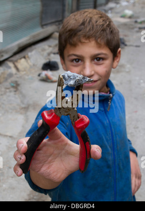 Ottobre 23, 2012 - Aleppo, Siria: un bambino tiene un caldo pezzo di metallo da un serbatoio di shell in Karmal AL Jabal. Foto Stock