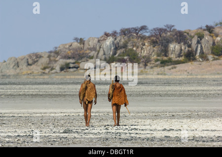 San bushman trackers attraversando a piedi il incrinato pan verso l'antico affioramento di granito di Kubu Island (Lekhubu), Makgadikgadi Pan, Botswana Foto Stock