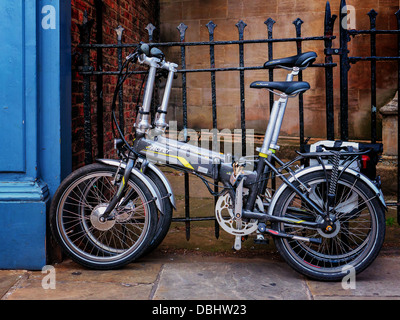 Due biciclette pieghevoli biciclette incatenati contro una black metal recinto nel centro di York, UK. Foto Stock