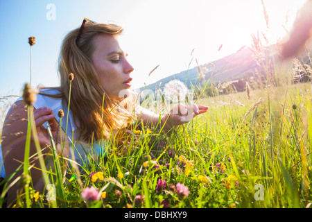 Ragazza adolescente seduto in un campo erboso soffiando a un seme dandilion testa. All'esterno. L'estate. Foto Stock