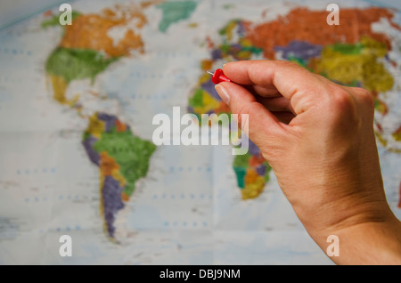 Mano con un perno rivolto a una mappa del mondo Foto Stock