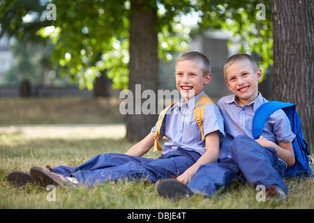 Immagine di felice twin ragazzi con zaini in seduta d'estate il parco Foto Stock