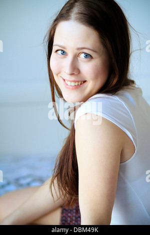 Donna con capelli castani si siede sul letto sorridente, Copenhagen, Danimarca Foto Stock