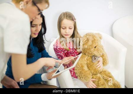 Medico donna e donna che guarda la tavoletta digitale, ragazza tenendo un orsacchiotto di peluche, osijek, Croazia Foto Stock