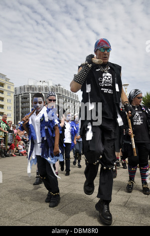 Il Gong spugnette maniaco Morris on Tour ballerini con i bambini in un misto di morris sul fronte mare durante Eastbourne Lammas Festival Foto Stock