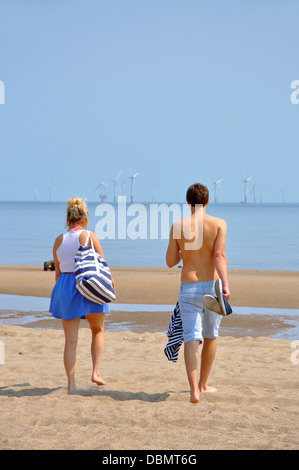 Coppia giovane camminando sulla spiaggia verso il mare, Skegness, Lincolnshire, England, Regno Unito Foto Stock