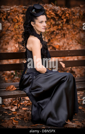 Giovane donna in stile gotico Moda seduta su una panchina in foresta, Croazia, Europa Foto Stock