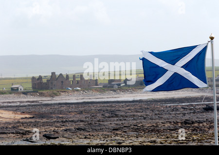 Una bandiera scozzese volando sulle isole Orcadi con le rovine del Palazzo Ducale a Birsay in background Foto Stock