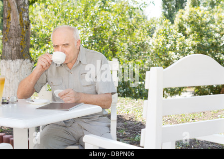 Uomo in pensione gustando una tazza di caffè seduti all'ombra di un albero a un cafe' all'aperto Foto Stock