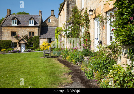 Il miele-lapidato cotswold cottage con rose e fiori estivi, accanto al villaggio verde a Stanton, Gloucestershire, Inghilterra Foto Stock