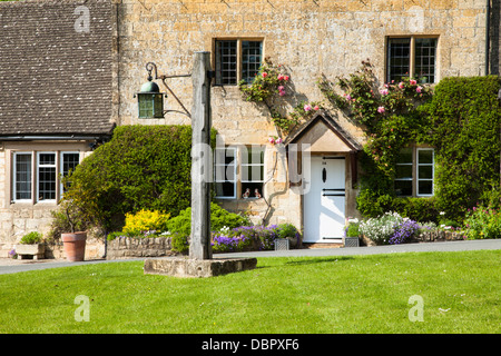 Un tipico a base di miele e lapidato Cotswold cottage con rose intorno al suo sportello accanto al villaggio verde, Stanton, Gloucestershire, Inghilterra Foto Stock