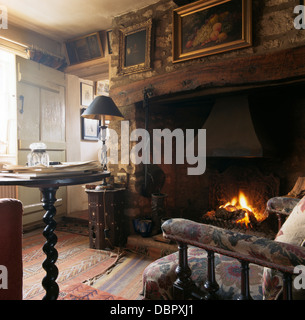 Le immagini sulla parete sovrastante camino inglenook in vecchio stile soggiorno con piccolo tavolo antico accanto Edwardian sedia Foto Stock