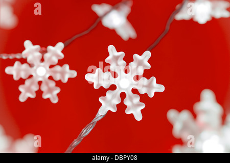 Il simbolo del fiocco di neve a forma di luci fairy contro uno sfondo di colore rosso. Foto Stock
