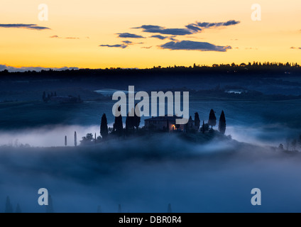 Agriturismo in Toscana nella nebbia mattutina con giallo cieli, Val d'Orcia, Italia Foto Stock