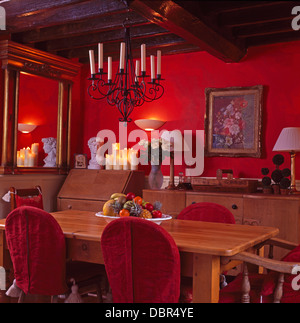 Ferro battuto lampadario di candela al di sopra di semplice legno tavolo e sedie con rosso copre allentati nel colore rosso brillante paese sala da pranzo Foto Stock
