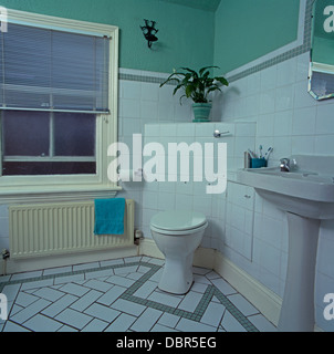 Tenda a veneziana sulla finestra sopra il radiatore accanto all angolo-set da toilette in bagno di colore verde con pareti piastrellate di bianco e pavimento Foto Stock