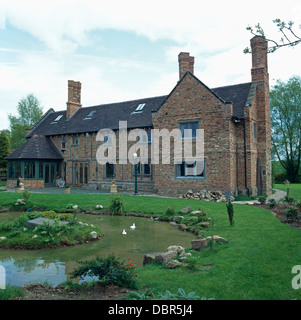 Laghetto circolare nel prato di fronte a nuove grandi-build, casa di campagna costruita in stile Tudor Foto Stock