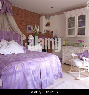 Coronet con crema voile oscuranti sopra il letto con testiera malva e copertura per il letto in stile cottage con camera da letto esposta parete di mattoni Foto Stock