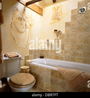 In piastrelle di pietra e parete vasca circondano in paese bagno con trompe-l'oeil testa romana dipinto sul muro Foto Stock