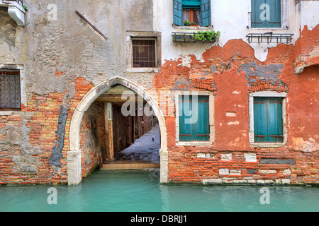 Stretto canale e la facciata della vecchia casa in mattoni rossi con ante chiuse a Venezia, Italia. Foto Stock