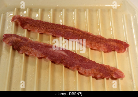 Due fette di tacchino cotto bacon siede su un piatto microondabili. Foto Stock