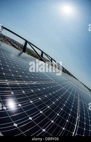 Profilo industriale del telaio in acciaio ad array solare sul tetto | Una vista fisheye cattura un array fotovoltaico sul tetto che si estende verso un orizzonte industriale, mentre il suo telaio di montaggio in acciaio cattura il sole in un'esplosione di luce. Gli impianti solari sui tetti generano elettricità nel punto di utilizzo, evitando le perdite di trasmissione che derivano dal trasporto di corrente da impianti solari a terra su larga scala e su lunghe distanze. Le celle in silicio monocristallino convertono la luce solare direttamente in energia. Foto Stock