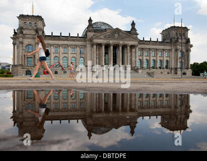 Una donna cammina passato l'Edificio del Reichstag, che si riflette in una pozzanghera a Berlino, Germania, 25 luglio 2013. Foto: Marcel Kusch Foto Stock