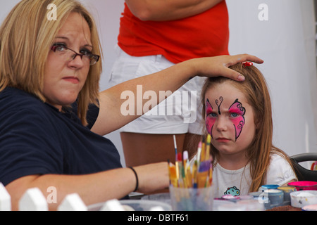 Face painting - pittura donna pink butterfly design sul viso della bambina Foto Stock