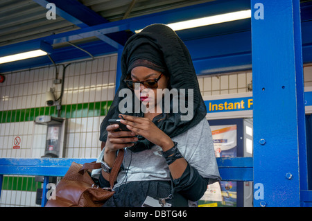 Una giovane donna etnica, in abito tradizionale, studiando il suo telefono cellulare a Croydon alla stazione degli autobus di Londra, Inghilterra, Regno Unito. Foto Stock