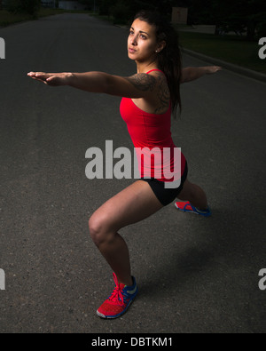 Giovane donna runner in Warrior II posa sulla strada della città Foto Stock