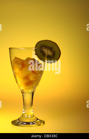 Vetro con ananas tagliata a cubetti e kiwi con uno sfondo giallo Foto Stock