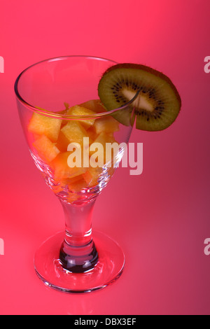 Vetro con ananas tagliata a cubetti e kiwi con un sfondo rosa Foto Stock