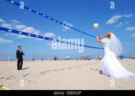 Una buffa sposa sposa e lo sposo giocare a pallavolo sulla spiaggia dopo il Jersey Shore matrimonio sulla spiaggia Foto Stock